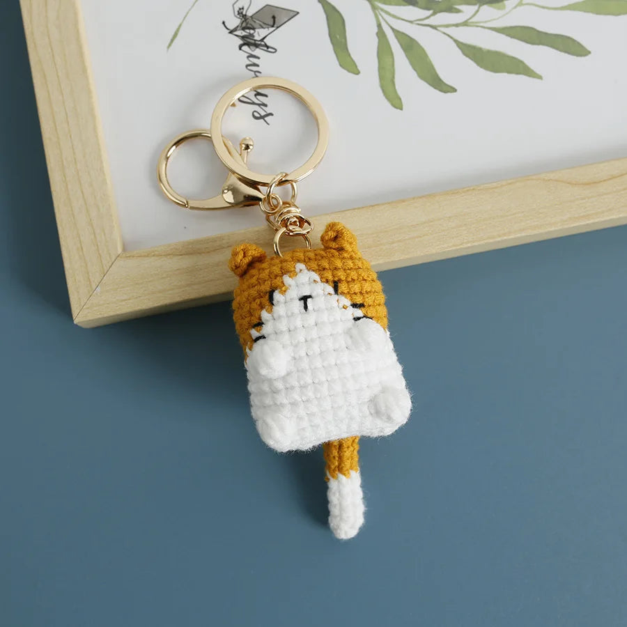 A handcrafted crochet cat keychain pendant with orange and white fur, attached to a gold ring.