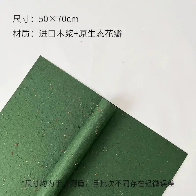 A sheet of dark green decorative packaging paper with dried flower petals rolled up.