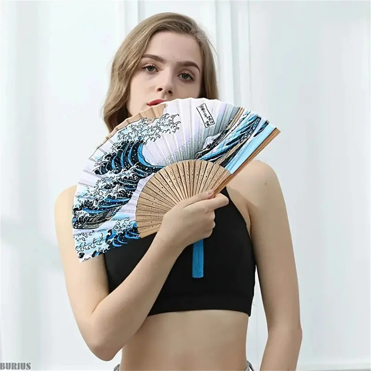 A woman holds a Japanese foldable hand fan featuring a Kanagawa wave design.
