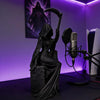 A black figurine of a gothic female grim reaper with a scythe is displayed under purple lighting.