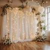 Elegant white wedding tulle backdrop decorated with floral greenery and warm string lights