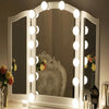 A white framed vanity mirror with round LED lights reflecting a silver chair and floral arrangements.