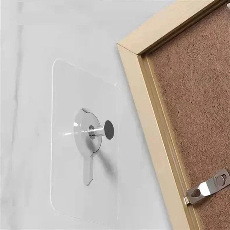 A close-up view of a silver adhesive wall hook mounted on a white surface next to a wooden frame.