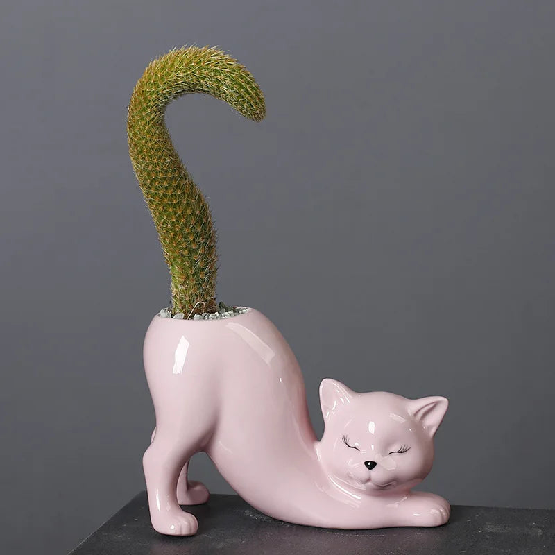 A pink ceramic cartoon cat planter holding a green succulent plant with a curved tail design.