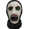 A grayscale mask resembling a grotesque face with glowing green eyes and an open mouth, worn as carnival headgear.