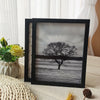 A black wooden photo frame displaying a grayscale silhouette of a bare tree against a misty landscape.