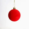 A bright red velvet flocked Christmas tree ornament hanging by a gold string.