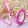 Pink satin balloon ribbon roll unwinding against a background of white flowers.