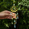 A hand holds a golden sun and crescent moon wind chime made of various colored crystals and beads.