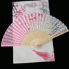 A vintage silk folding fan with pink and white floral patterns is displayed on a white background.