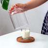 A hand pours a white candle into a glass aromatherapy holder with a wooden base and dust-proof cover.
