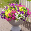 A vibrant artificial floral bouquet featuring mixed purple, yellow, and pink flowers in a gray pedestal planter.