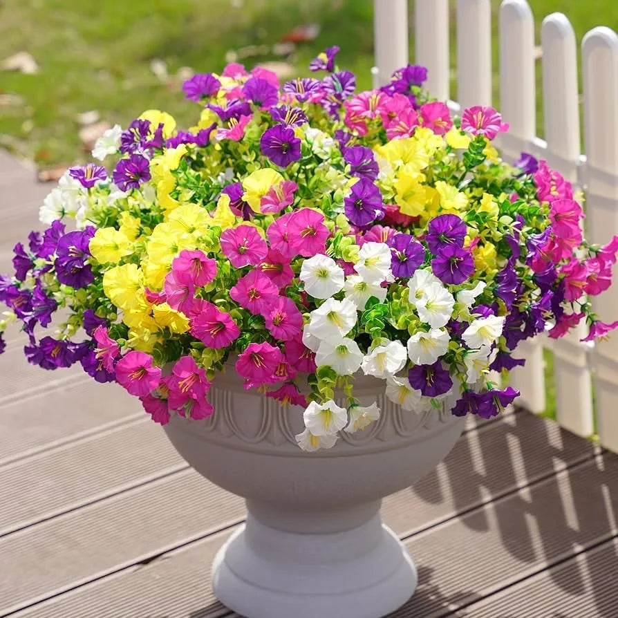 A vibrant artificial floral bouquet featuring mixed purple, yellow, and pink flowers in a gray pedestal planter.
