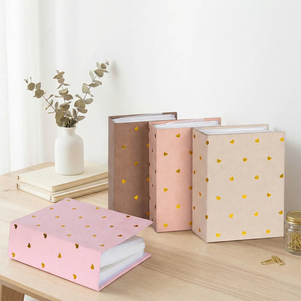 A stack of pink and beige photo albums with gold foil hearts resting on a wooden table.