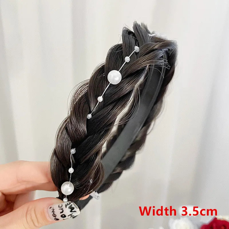 A hand holds a black hair band adorned with silver pearl-like bands and wispy dark hair.