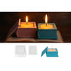 A lit candle in a pink holder rests on an open book, with an openable blue silicone mold beside it.