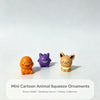 Three mini cartoon animal squeeze ornaments in orange, purple, and tan sitting on a white surface.