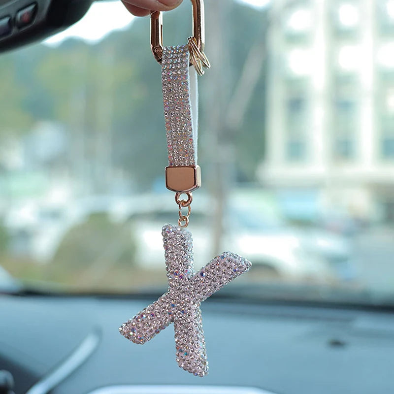 A close-up of a crystal letter keychain charm shaped like an X hanging from a gold-toned clasp.