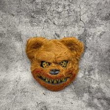 A fluffy orange bear face mask with glowing yellow eyes against a gray textured background.