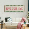 A framed canvas art print featuring the text LOVE YOU BYE in pink on a light background with a green border, displayed above 
