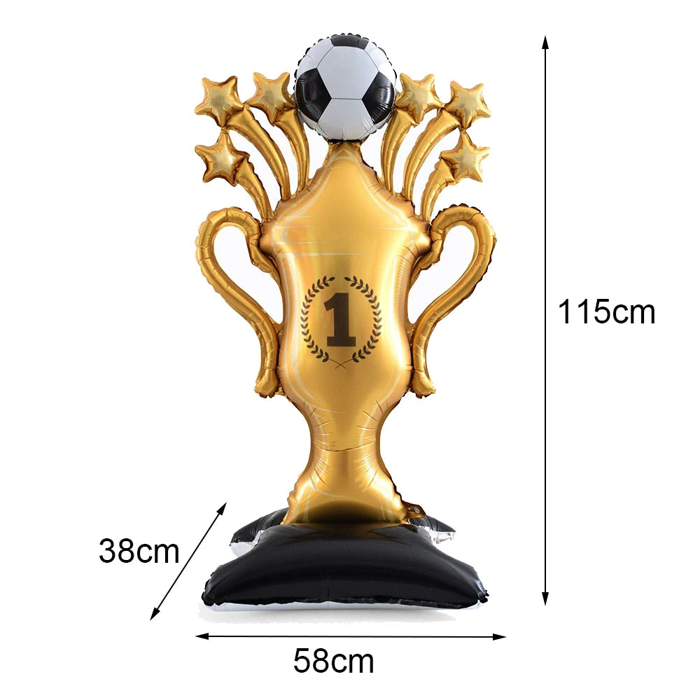 A gold standing soccer balloon trophy with a silver football on top, used as party décor.
