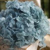 A bouquet of light blue dried hydrangea flowers displayed on a wooden surface.