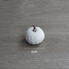 A single white velvet pumpkin decoration is shown on a gray wooden surface.