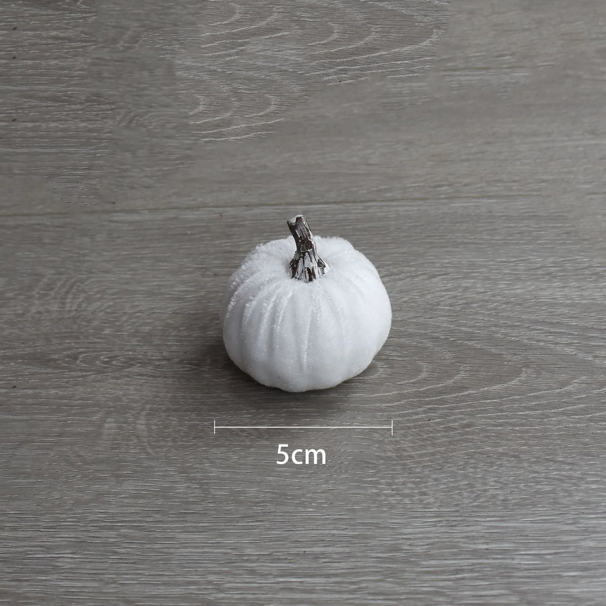 A single white velvet pumpkin decoration is shown on a gray wooden surface.