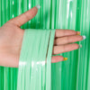 A hand holds a strand of metallic green tinsel foil fringe curtain backdrop.