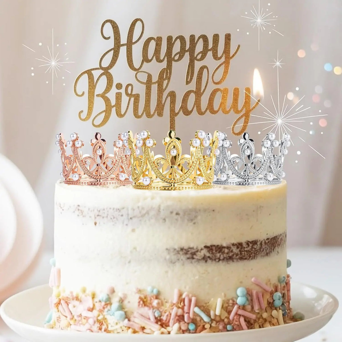 A white layer cake decorated with gold and silver pearl crown toppers and pink sprinkles.