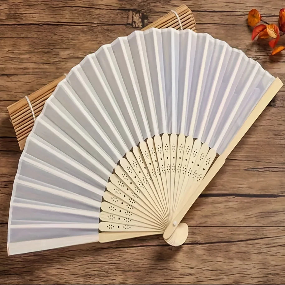 A white bridal handheld folding fan set with light wood accents is displayed on a wooden surface.