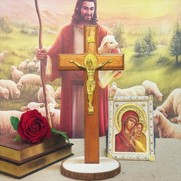 A wooden crucifix with a gold Jesus figure stands in front of a painting of Jesus and sheep.