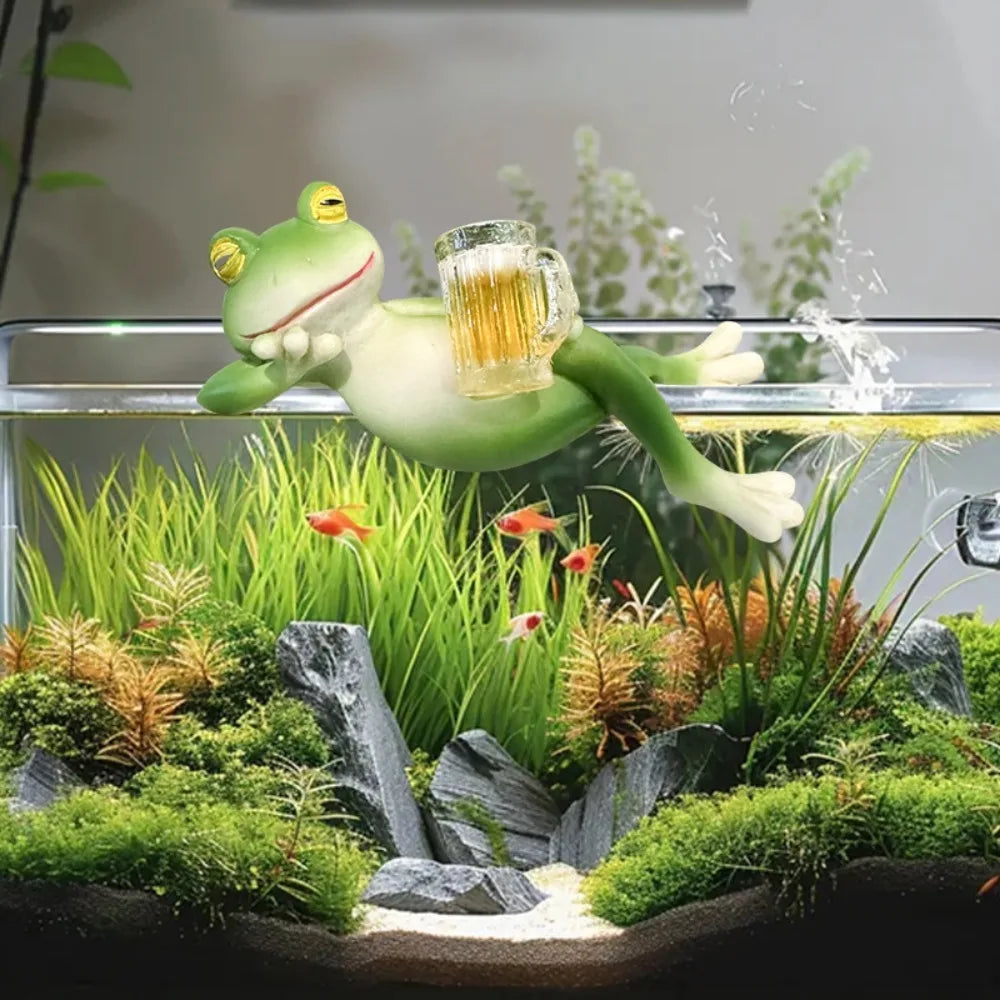 Una figura de rana de resina verde nadando en un tanque de vidrio lleno de plantas y rocas acuáticas.