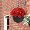 A hanging black basket filled with bright red artificial poinsettia flowers against a brick wall.