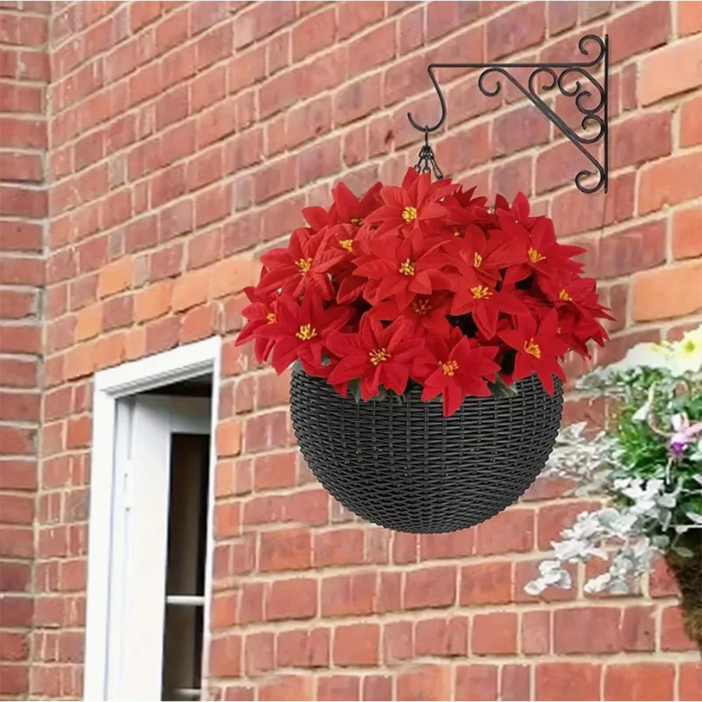 A hanging black basket filled with bright red artificial poinsettia flowers against a brick wall.
