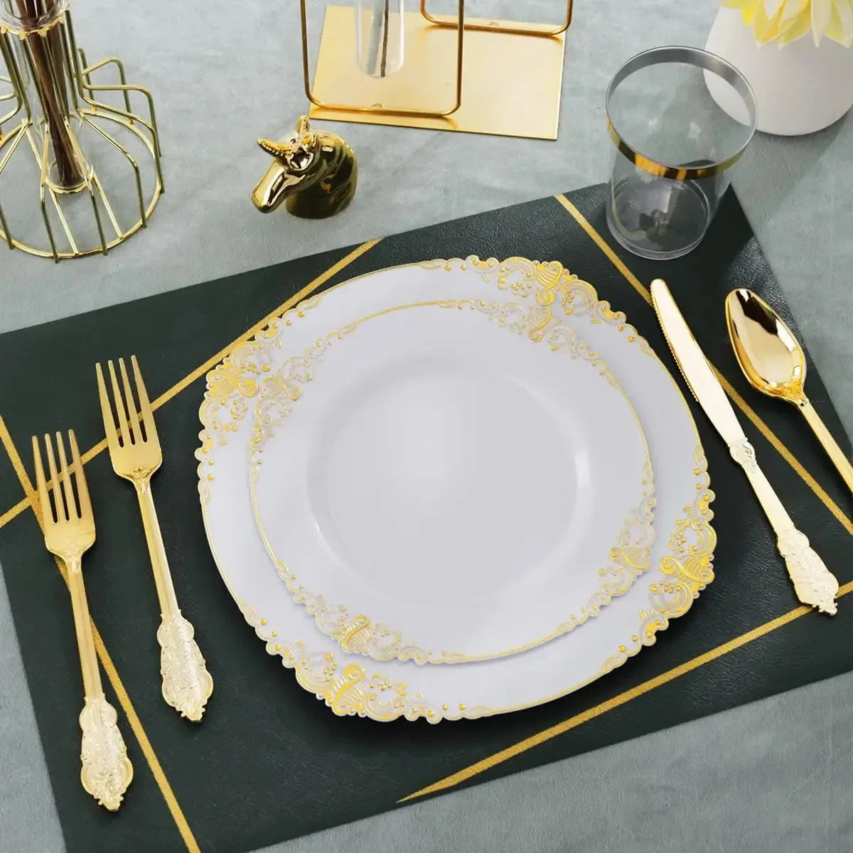 Elegant white and gold disposable dinnerware set with cutlery displayed on a dark green mat.