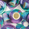 A purple and teal mermaid themed tableware set featuring plates, cups, and napkins.