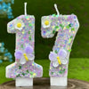 Two number candles, 1 and 7, decorated with purple glitter and white flowers and butterflies.