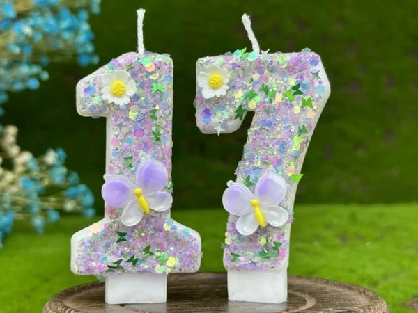 Two number candles, 1 and 7, decorated with purple glitter and white flowers and butterflies.
