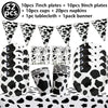 A collection of cow print tableware including plates, cups, napkins, a tablecloth, and a banner for a farm-themed party.