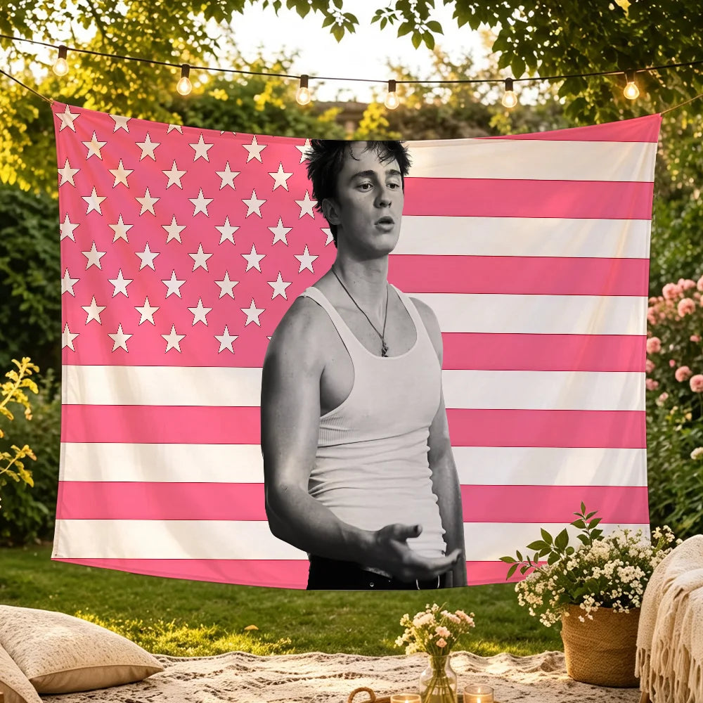 A man stands in front of a pink and white American flag tapestry hanging outdoors.