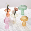 Collection de vases décoratifs en champignons de verre dans des tons rose, vert et ambre sur une nappe en dentelle blanche.