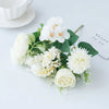 A bouquet of white artificial silk peony flowers with green leaves and a small card on a white surface.