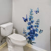 A wall decal featuring a cluster of blue flowers and butterflies on a white wall above a toilet.