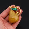 A golden pear-shaped charm with a green gemstone is held in a hand.