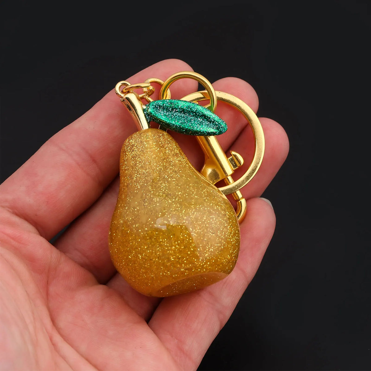 A golden pear-shaped charm with a green gemstone is held in a hand.