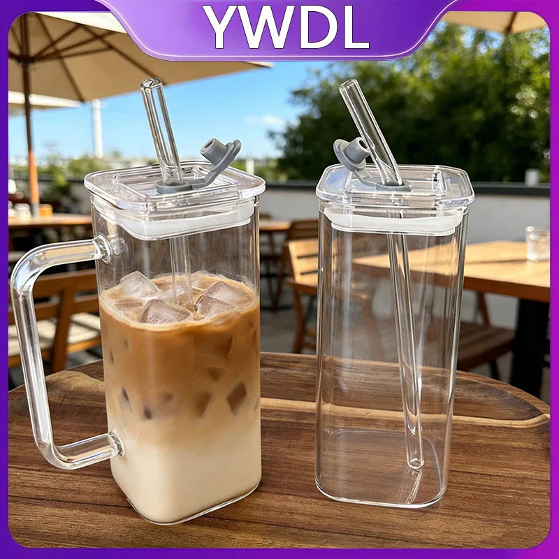 A clear glass insulated coffee mug filled with iced latte, featuring a metal lid and straw, set on a wooden table.