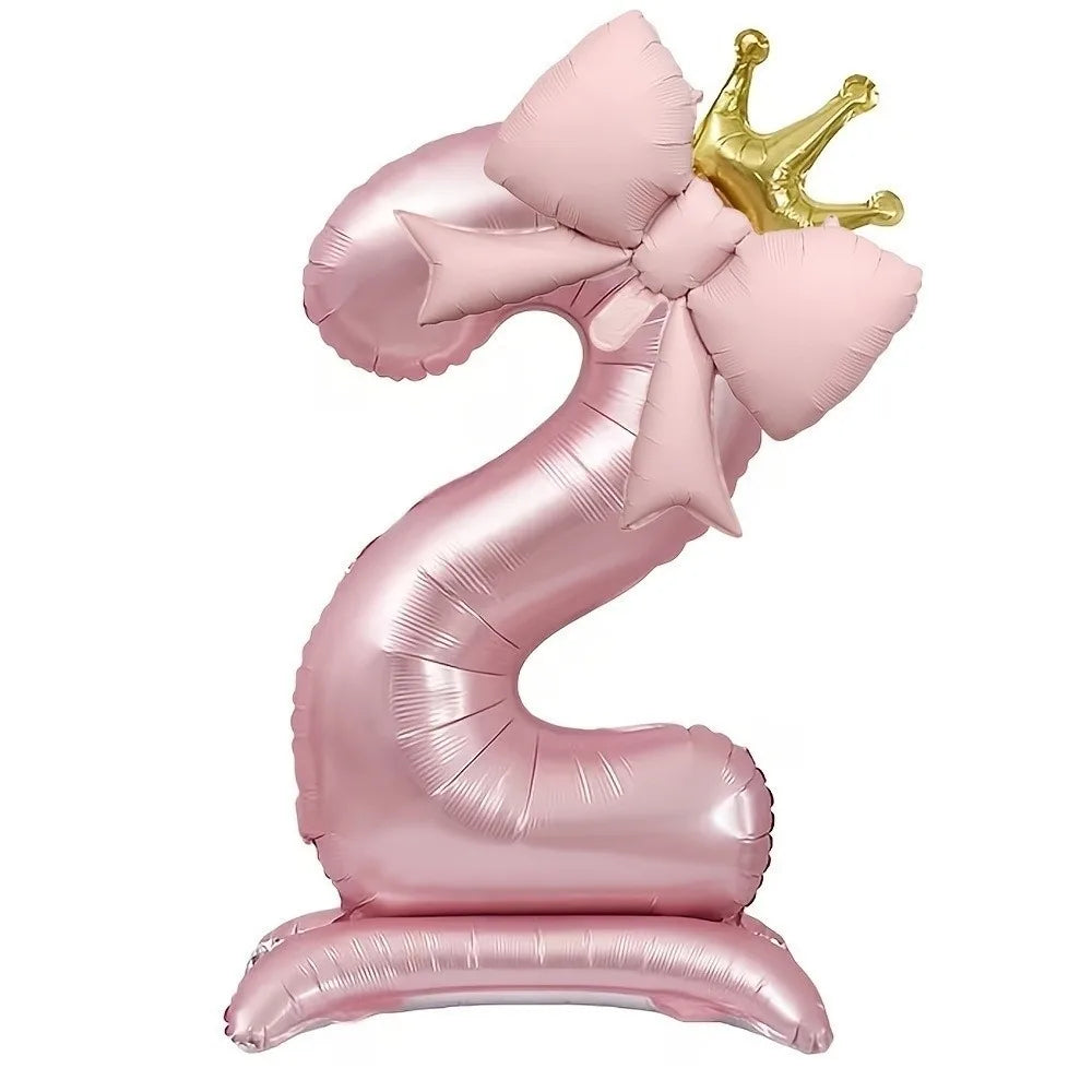 A pink foil balloon shaped like the number 9, decorated with a bow and topped with a gold crown.