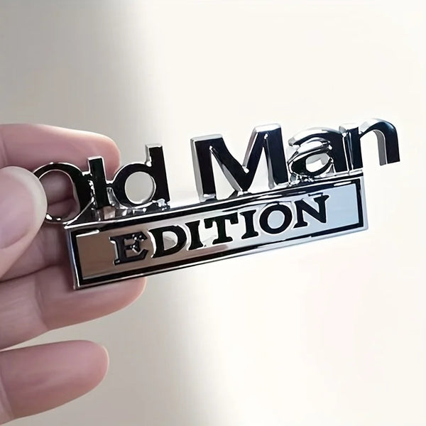 Une main tient un emblème en métal argenté avec l'inscription Old Man Edition gravée.