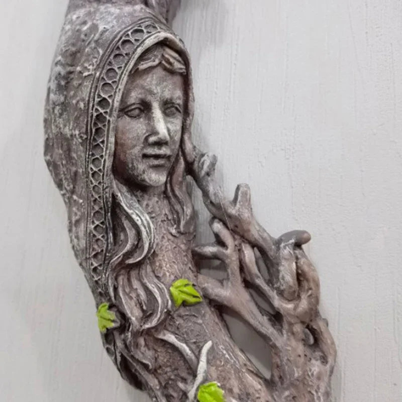 A textured, gray wall hanging featuring a face emerging from tree roots and leaves.